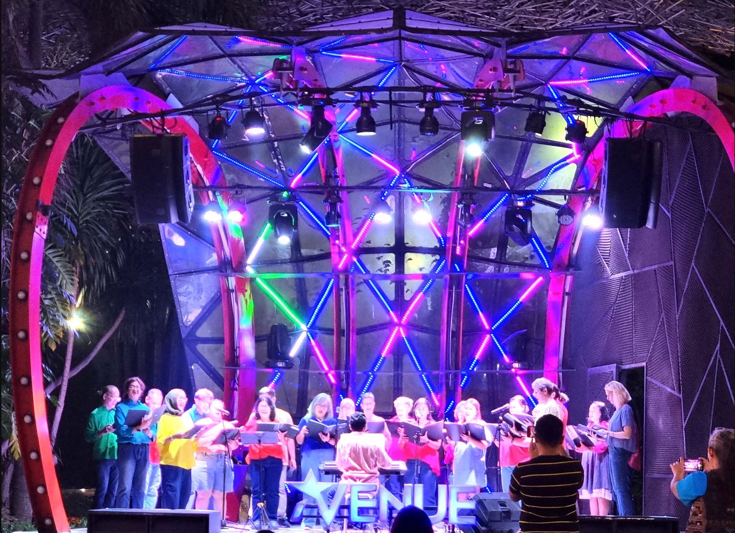 SJCC performing on a colourfully lit outdoor stage